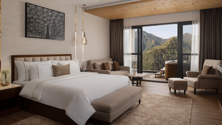A spacious luxury bedroom with a large double bed, comfortable armchairs, and glass doors opening to a forest view.
