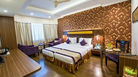 Grand Room with twin bed and seating area on the side with a fan on the ceiling at Swosti Grand, Bhubaneswar