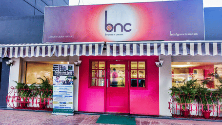 Facade of Brown N Cream with plants on the side of the entrance at Swosti Grand, Bhubaneswar