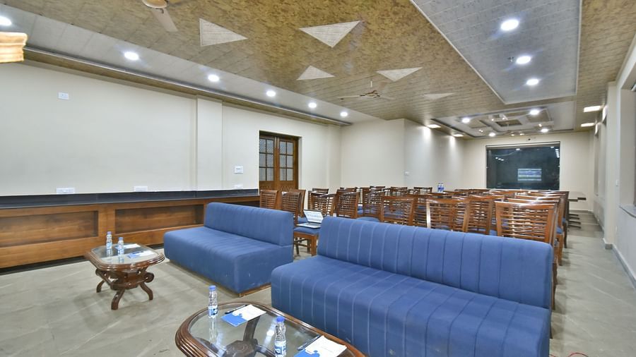 A banquet hall with a blue sofa and wooden chairs facing the podium at DLS Ark Holiday Inn, Banikhet.