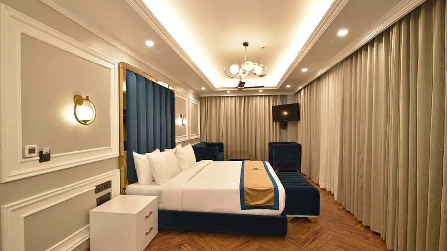 A spacious hotel room with a large bed, contemporary decor, and a cosy seating area. Large windows allow natural light and offer scenic mountain views.