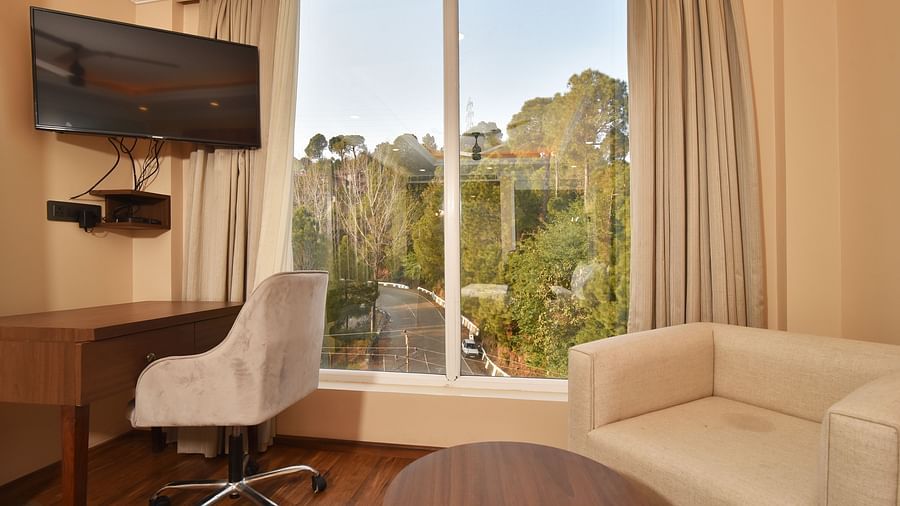 A modern seating area with a comfortable sofa, a work desk, and large windows providing a clear view of the surrounding landscape and mountains.