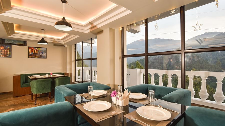  A contemporary dining space with teal chairs, a table set with plates, and large windows framing a picturesque view of the surrounding mountain scenery.