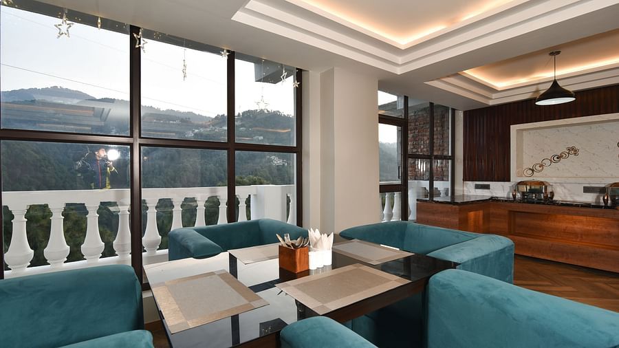 A stylish dining area with teal upholstered chairs, a table set for two, and large windows offering scenic views of the surrounding hills.