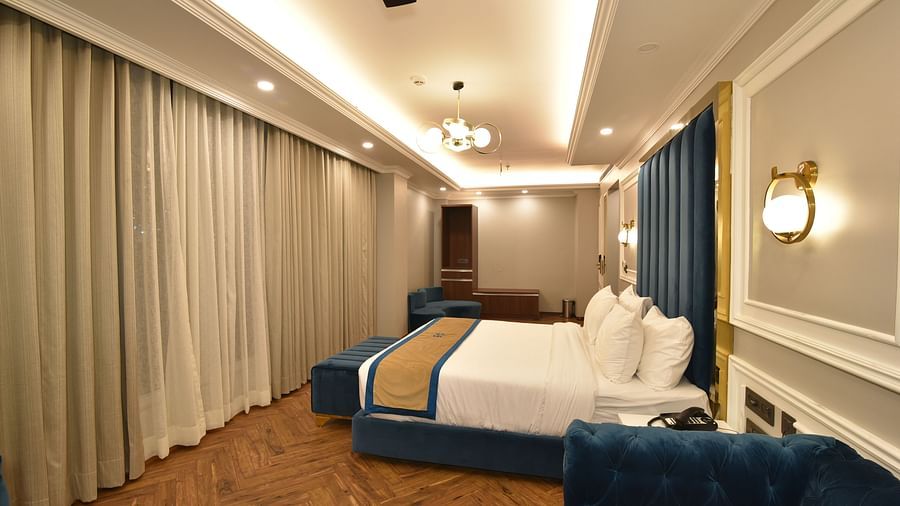 A stylish bedroom with a large bed and a seating area. The room features soft lighting, with large windows showcasing panoramic views of the surrounding hills.