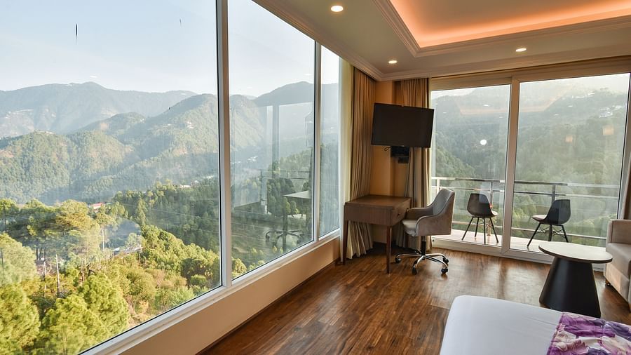 A modern bedroom with a king-sized bed, a seating area by the window, and large glass windows providing expansive views of the mountains.
