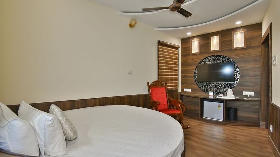 A Deluxe Room at DLS Dalhousie Valley Resort with a round  king size bed, mirror and a resting chair.