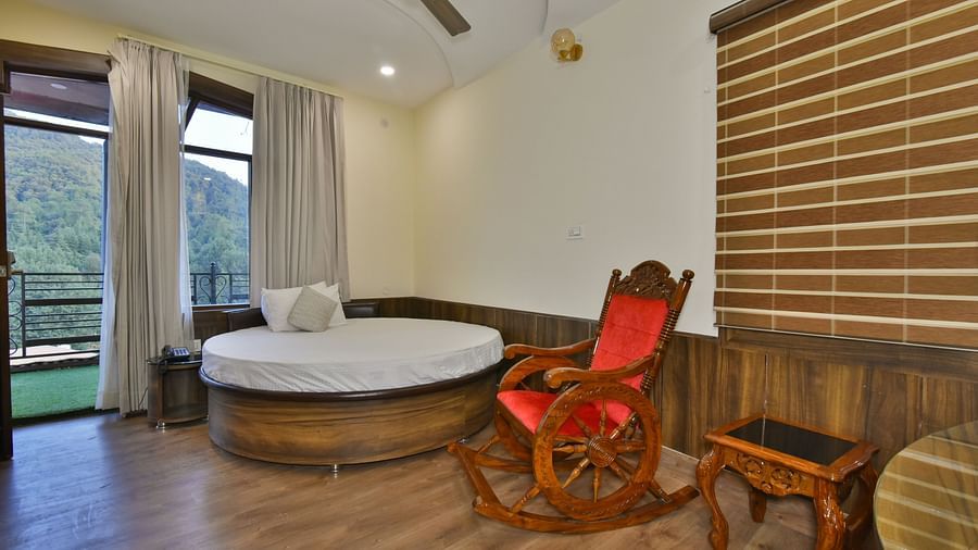A Deluxe Room at DLS Dalhousie Valley Resort with a round king size bed, a chair and a balcony 