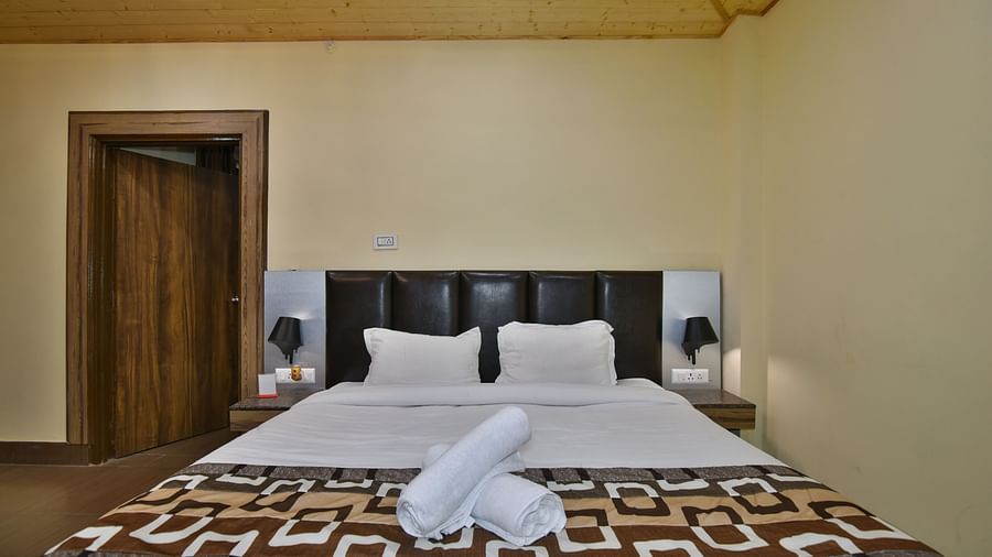 A Deluxe Room at DLS Dalhousie Valley Resort with a  king size bed and towels kept on them.