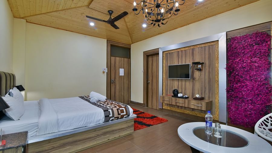 Sideview of a Deluxe Room at DLS Dalhousie Valley Resort with a  king size bed, TV and a table