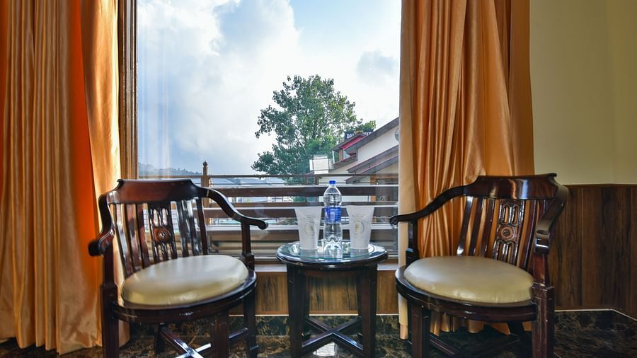 Sitting area of a Deluxe Room at DLS Dalhousie Valley Resort with brow chairs, a large window and a table.