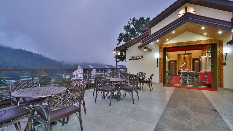Open terrace at DLS Dalhousie Valley Resort featuring chairs and tables with backdrop of misty mountains.