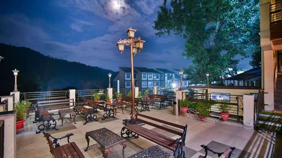Side view of open terrace at DLS Dalhousie Valley Resort featuring benches and tables during evening.