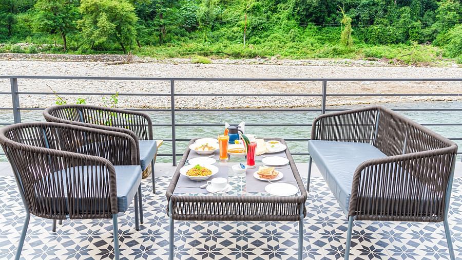 Various dishes plated and kept on the table of a restaurant at DLS Divine River Resort and Spa surrounded by lush greenery and river views.