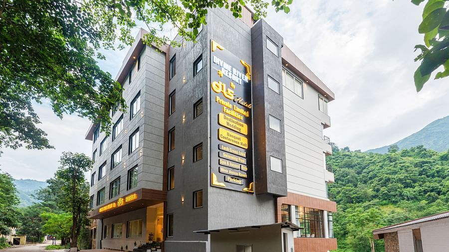 Facade of DLS Divine River Resort and Spa with backdrop of lush misty mountains.