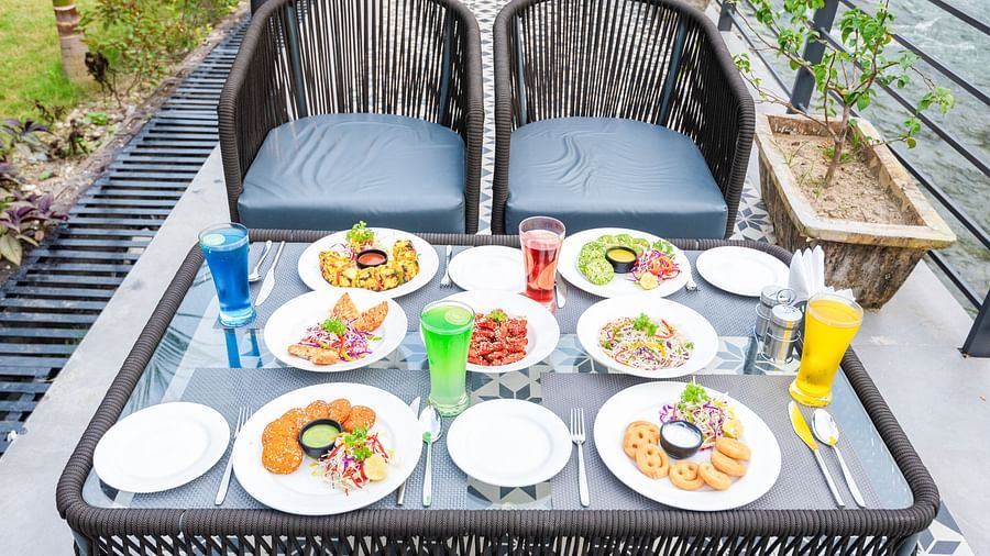 Various dishes plated and kept on the table of a restaurant at DLS Divine River Resort and Spa surrounded by lush greenery. 