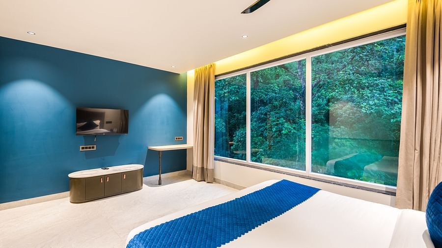 Deluxe Room at DLS Divine River Resort and  Spa featuring a  king bed, side table, TV and balcony with forest views.