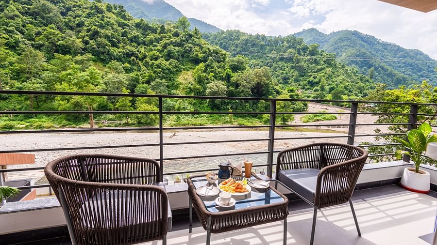 Balcony of Premium Room at DLS Divine River Resort and  Spa featuring seating area with food kept on table and backdrop of river and forest views.