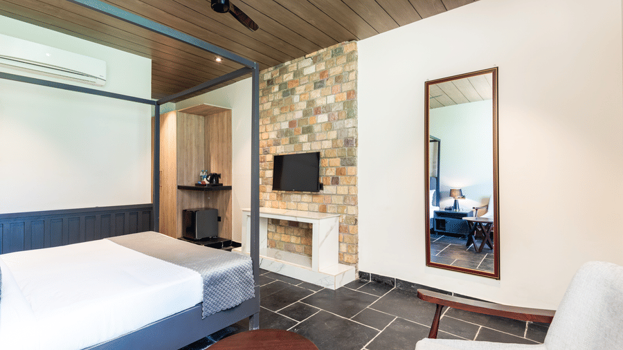 Bedroom of Luxury Cottage at DLS Divine River Resort and Spa, Rishikesh, featuring a king size bed with mirror, TV and a chair.