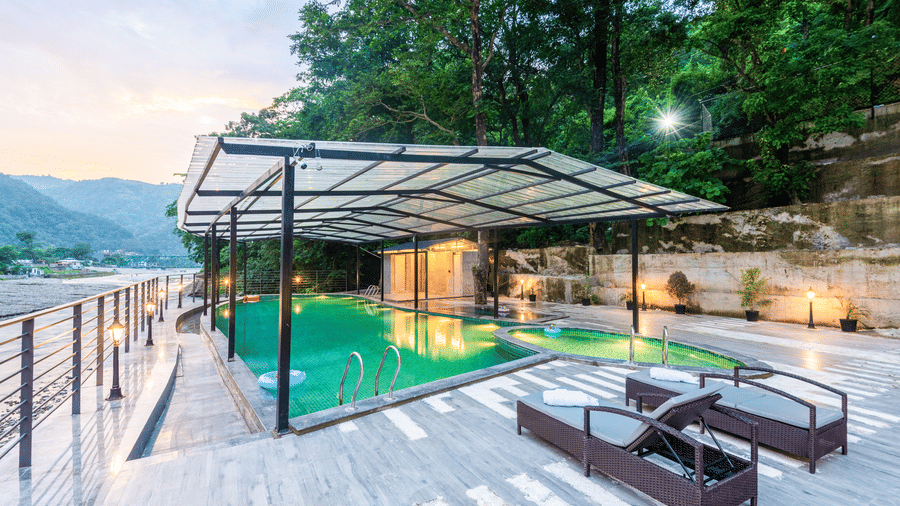 A swimming pool at DLS Divine River Resort and Spa, Rishikesh, with panoramic views of distant mountains and lounge chairs.
