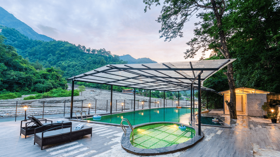 A swimming pool at DLS Divine River Resort and Spa, Rishikesh, with panoramic views of the distant mountains and lounge chairs. 