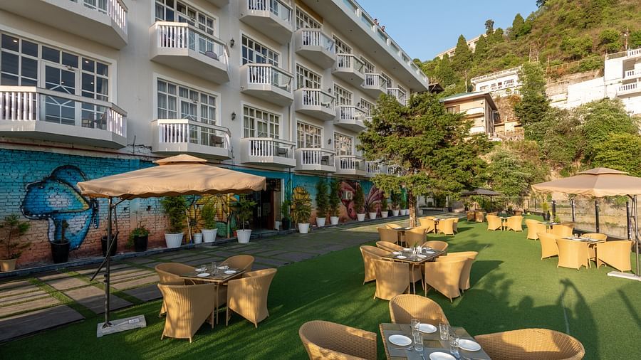 Facade view of DLS Highland Resort and Spa, Mussoorie with comfortable chairs in the lawn at dusk.
