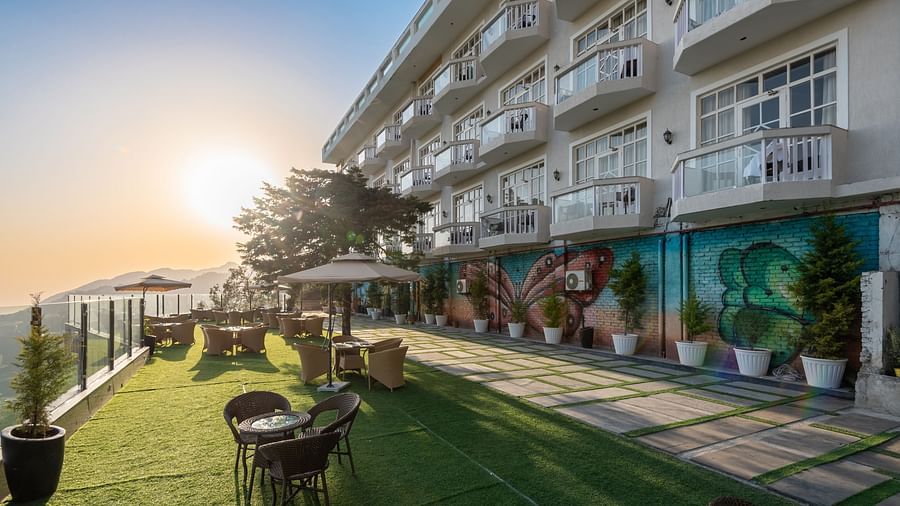 Facade view of DLS Highland Resort and Spa, Mussoorie with comfortable chairs in the lawn at dusk.