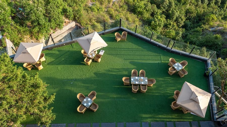 Aerial view of the lawn with comfortable seating surrounded by hills at Food and drinks placed on the table at DLS Highland Resort and Spa, Mussoorie.