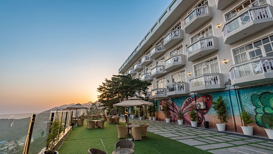 Facade view of DLS Highland Resort and Spa, Mussoorie with comfortable chairs in the lawn at dusk.