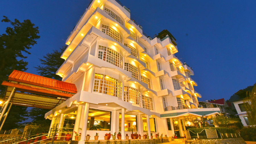 Exterior view of DLS Hillcrest Resort, Shimla, illuminated with warm yellow lights during the evening.