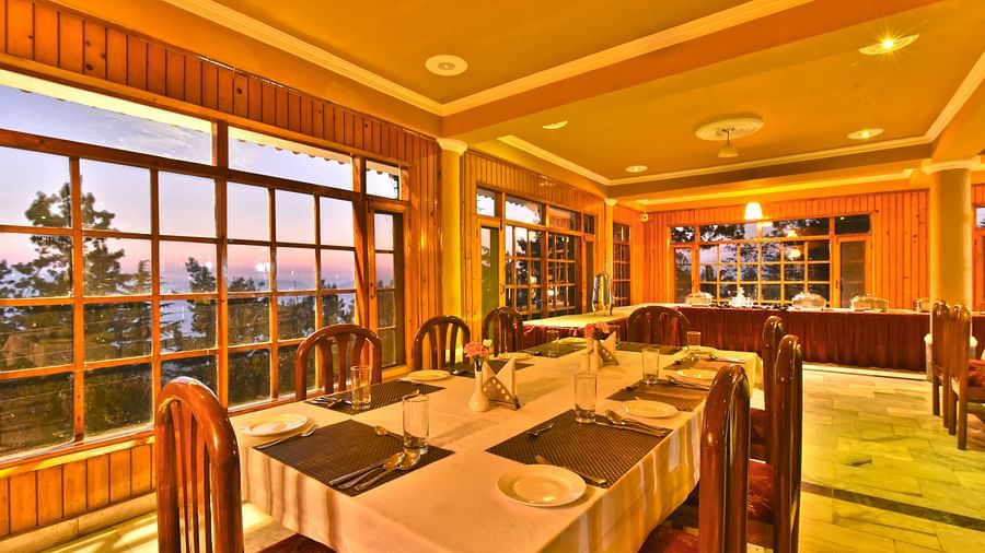 Restaurant with large windows offering scenic views at DLS Hillcrest Resort, Shimla.