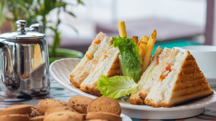 A neatly prepared sandwich platter with biscuits tea and tableware at DLS Hotels on the Ganges Rishikesh offering a simple yet fulfilling snack option enjoyed in a serene mountain facing dining space.
