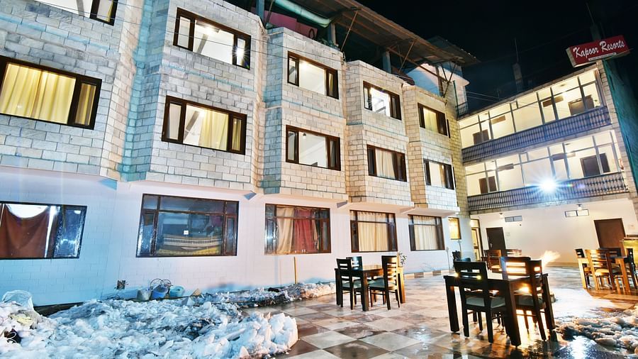 The exterior of DLS Kapoor Resorts Manali at night, showcasing its stone facade, outdoor dining area, and warm lighting.
