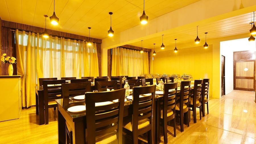 A shot of the dining table at the restaurant featuring woodden tables and chairs | DLS Kapoor Resort Manali