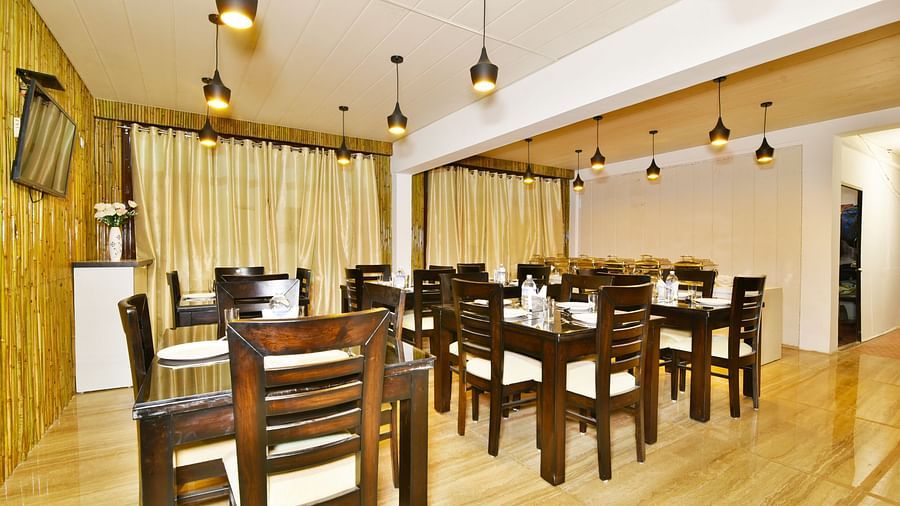 Dining area with woodden tables and chairs, yellow curtains, and pendant lights | DLS Kapoor Resort Manali