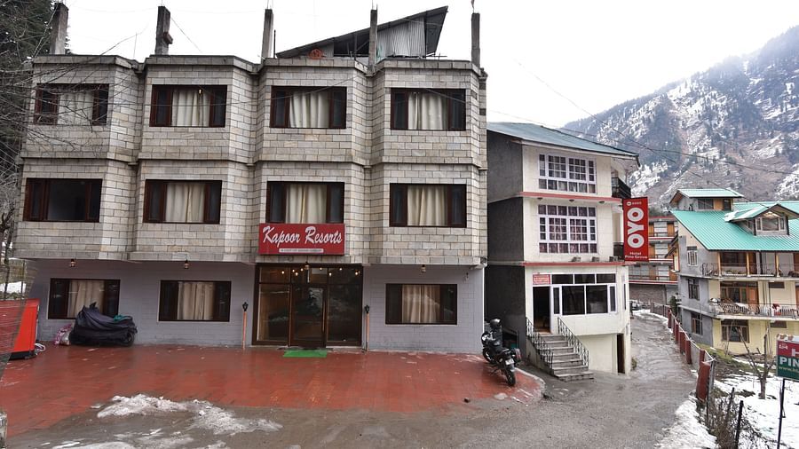 The image shows the front view of a hotel building that is multi storied with a flat roof and several windows | DLS Kapoor Resort Manali