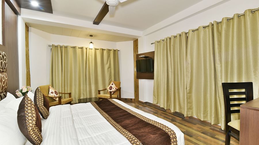 A close up shot a large room featuring king size bed, a side table and expansive windows with curtains | DLS Kapoor Resort Manali