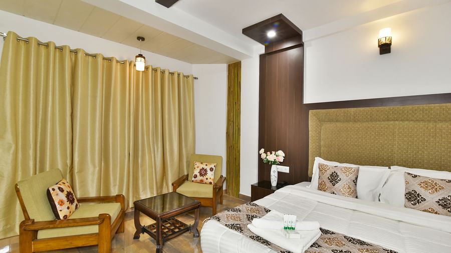 A closeup shot of the king size bed in a room that also features a cosy seating  | DLS Kapoor Resort Manali