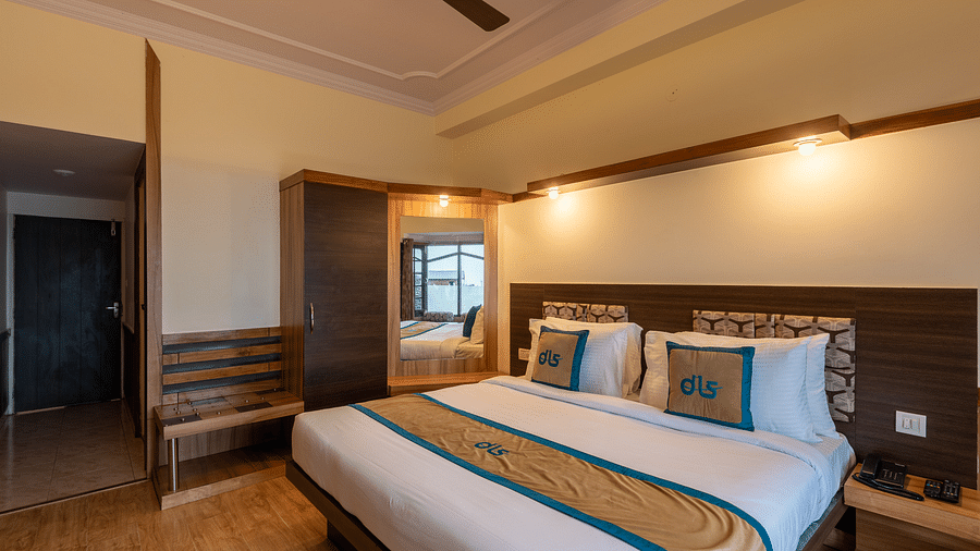Deluxe room with wooden flooring, a mirror, a wardrobe, and a bedside table with a fan and comfortable bedding - DLS Meghavan Resort, Dharamshala
