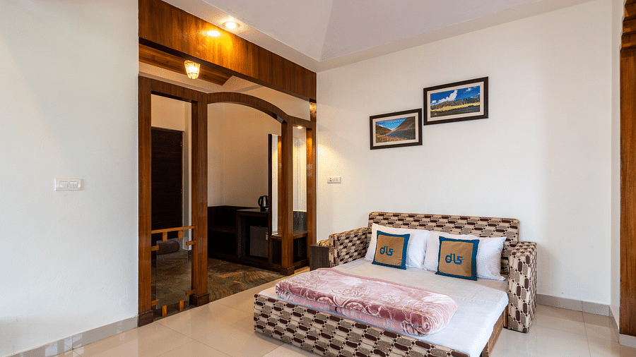 A room with a cosy seating area, a small table, and framed pictures on the wall. The room has a fan and a view into the adjacent area - DLS Meghavan Resort, Dharamshala