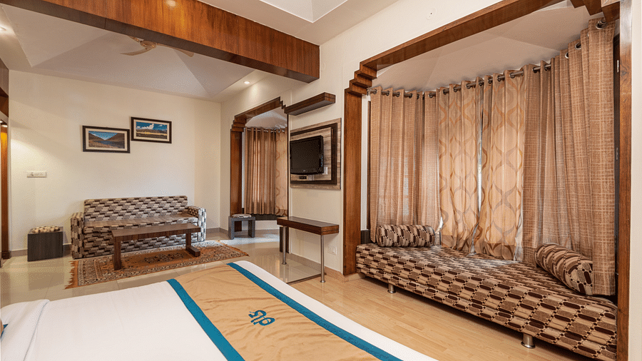 A junior suite with a bed, wooden ceiling, cosy seating, TV, and elegant window detailing, offering a spacious and comfortable atmosphere - DLS Meghavan Resort, Dharamshala