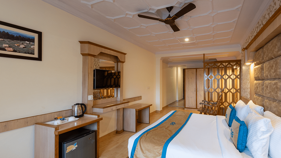 A premium room with a bed, wooden decor, TV, seating area, and scenic views, offering a relaxing and comfortable stay - DLS Meghavan Resort, Dharamshala
