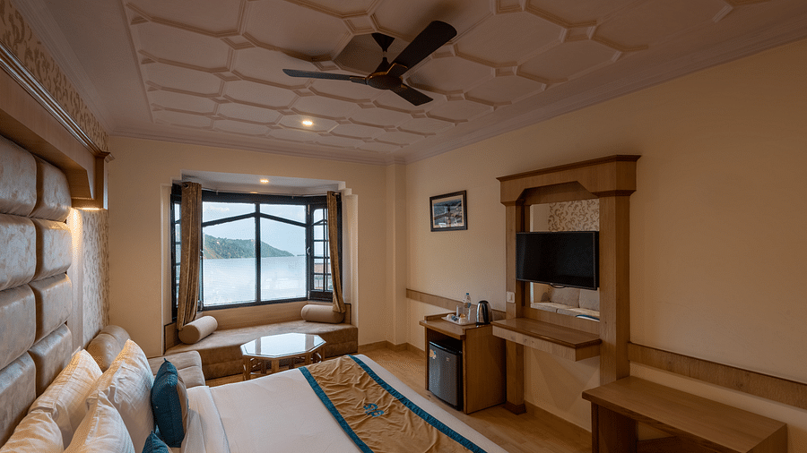 A premium room with a comfy bed, wooden accents, a flat-screen TV, and scenic window views, offering a relaxing and spacious stay - DLS Meghavan Resort, Dharamshala