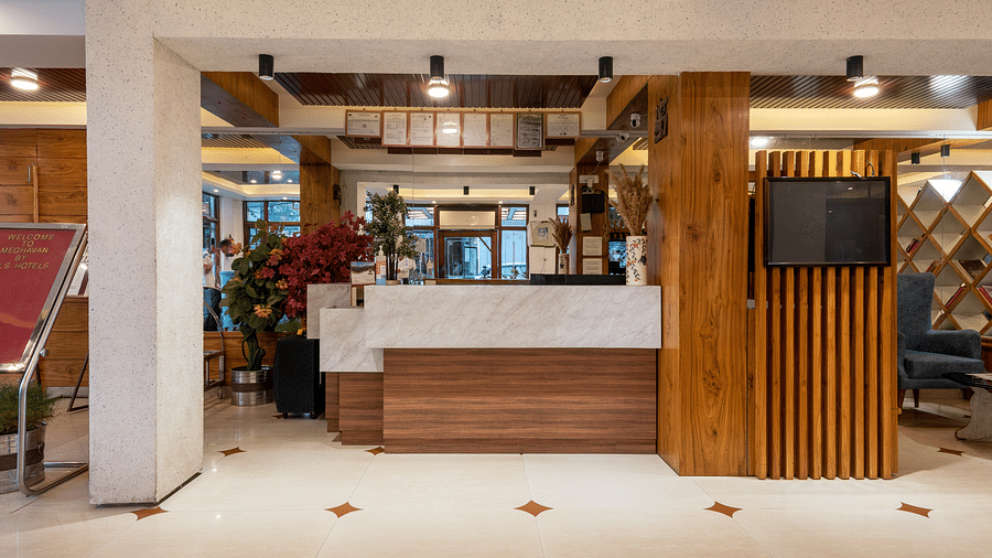 A hotel reception area featuring a welcome sign, plants, a marble and wood reception desk, and a TV mounted on the side - DLS Meghavan Resort, Dharamshala