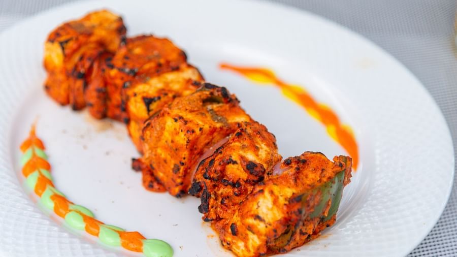 Cubes of orange-red, char-grilled paneer threaded like a kebab on a white plate, accented with decorative streaks of orange and green sauce - DLS Nature Trinket Resort, Dalhousie.