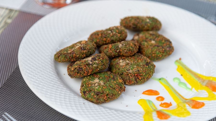 Close-up of a white plate with a neatly arranged serving of green vegetable cutlets, garnished with colourful sauce drizzles on the side - DLS Nature Trinket Resort, Dalhousie.