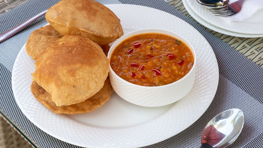 A plate of fluffy puris served with a bowl of spicy chole (chickpea curry), garnished with chopped red peppers - DLS Nature Trinket Resort, Dalhousie.