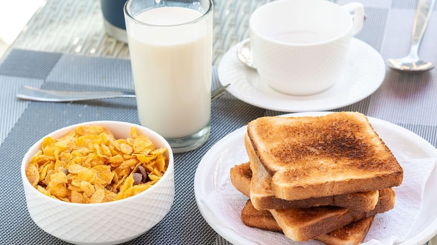Continental breakfast spread with a bowl of cornflakes, a stack of toasted bread, a glass of milk, and a cup of tea or coffee placed on a glass table - DLS Nature Trinket Resort, Dalhousie.