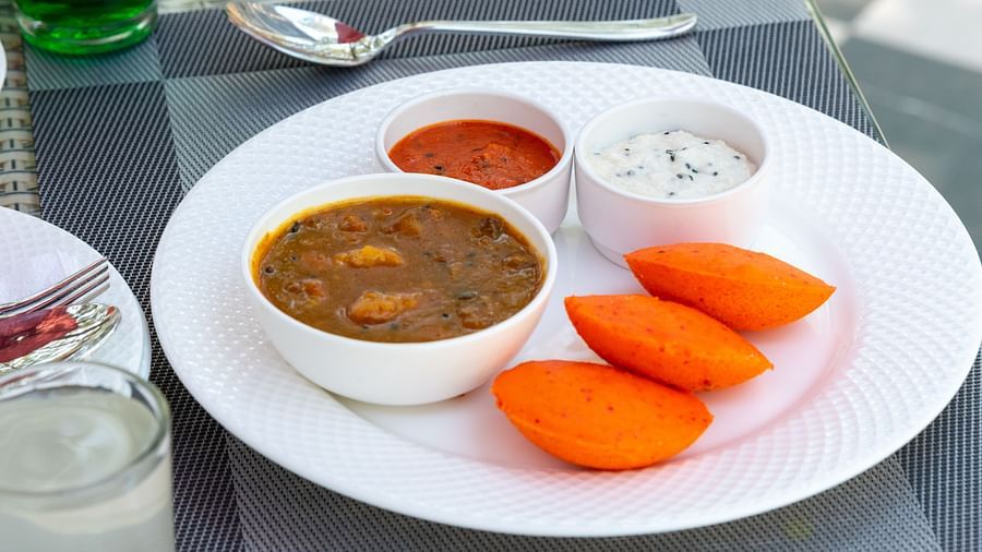 South Indian breakfast plate with three orange idlis, served alongside bowls of sambar, coconut chutney, and tomato chutney on a white plate - DLS Nature Trinket Resort, Dalhousie.