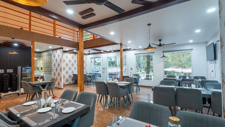 Contemporary restaurant dining area with neatly set tables, cushioned chairs, ceiling fans, and large windows providing natural light - DLS Nature Trinket Resort, Dalhousie.